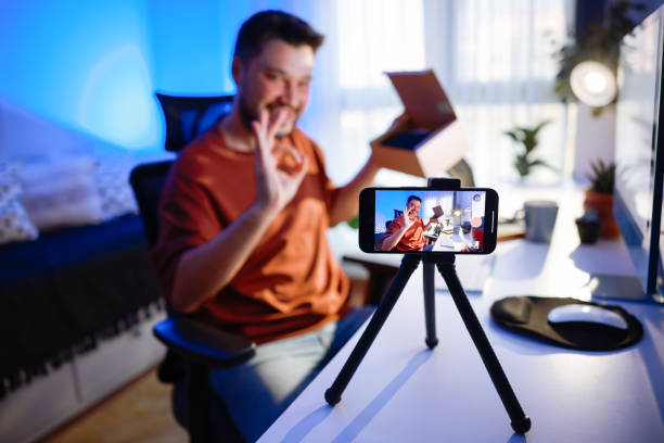 istock Male blogger unboxing parcel with tech product using smartphone on tripod, recording video content for tech blog at home 2195908951
