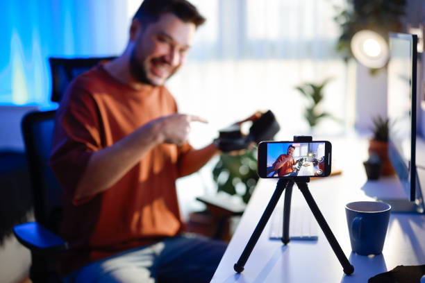 istock Male blogger unboxing parcel with tech product using smartphone on tripod, recording video content for tech blog at home 2195922839
