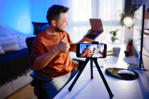 istock Male blogger unboxing parcel with tech product using smartphone on tripod, recording video content for tech blog at home 2195923244