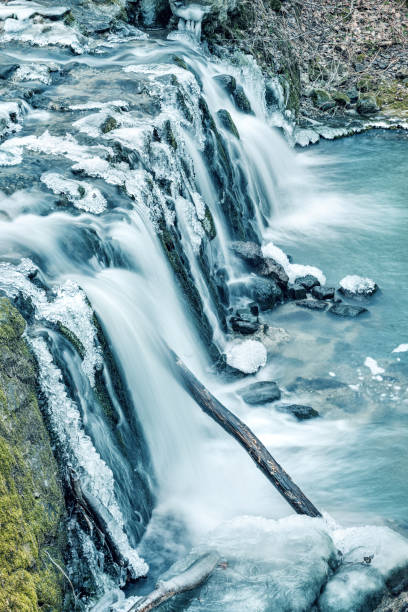 Icicles hang from the side of a waterfall, creating a stunning winter scene. The waterfall is located in a mountainous area, and the rocks are covered in ice. Hungary