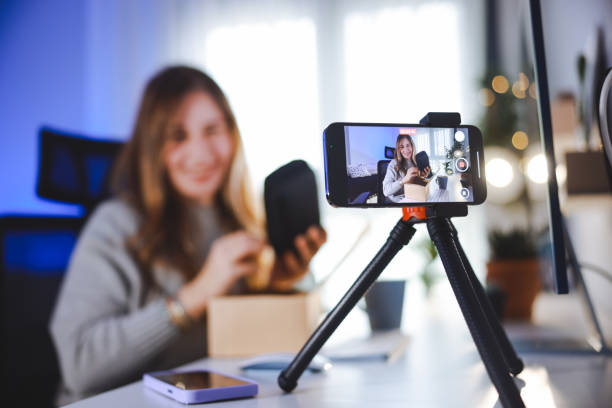 istock Female blogger unboxing parcel with tech product using smartphone on tripod, recording video content for tech blog at home 2195923996