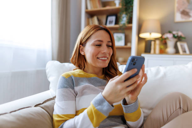 istock Happy woman using mobile phone while relaxing on sofa at home 2195924070