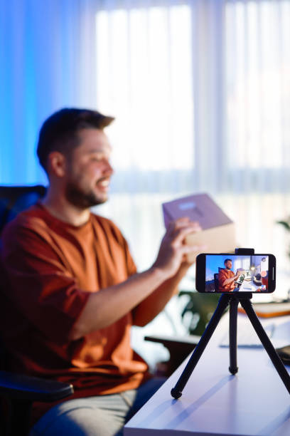istock Male blogger unboxing parcel with tech product using smartphone on tripod, recording video content for tech blog at home 2195924113