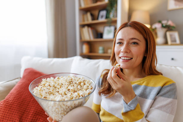 istock Smiling woman eating popcorn while watching a movie at home 2195924264