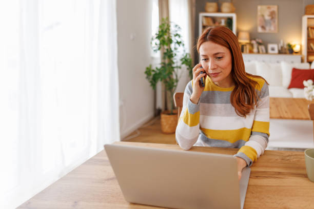 istock Focused young woman working from home, talking on the phone and using laptop 2195924277