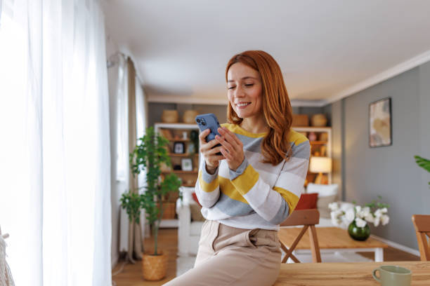 istock Woman using smartphone and smiling while sitting on table at home 2195924309