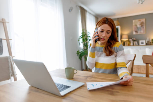 istock Focused businesswoman talking on phone and analyzing documents while working from home 2195924339