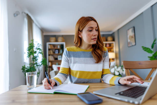istock Focused businesswoman working from home taking notes while looking at laptop 2195924357