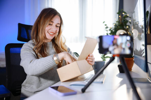 istock Female blogger unboxing parcel with tech product using smartphone on tripod, recording video content for tech blog at home 2195924600