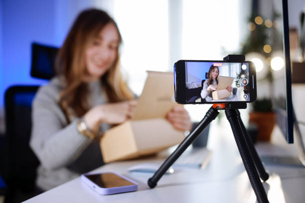 istock Female blogger unboxing parcel with tech product using smartphone on tripod, recording video content for tech blog at home 2195928375