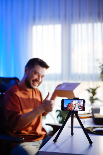 istock Male blogger unboxing parcel with tech product using smartphone on tripod, recording video content for tech blog at home 2195928439