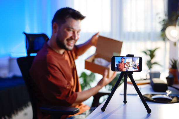 istock Male blogger unboxing parcel with tech product using smartphone on tripod, recording video content for tech blog at home 2195928592