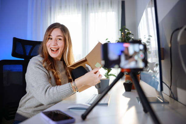 istock Female blogger unboxing parcel with tech product using smartphone on tripod, recording video content for tech blog at home 2195929116