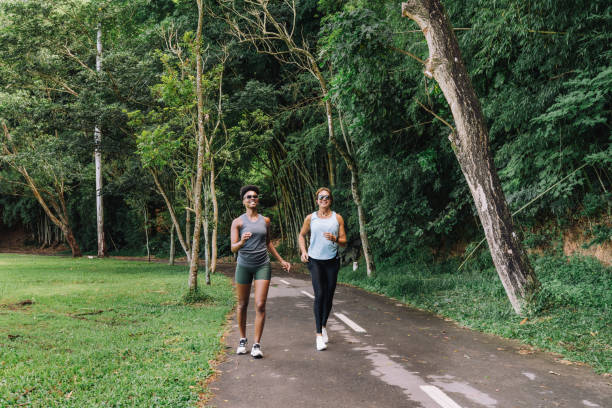 istock Two women jogging on an asphalt path by a lush forest at a public park 2195932153