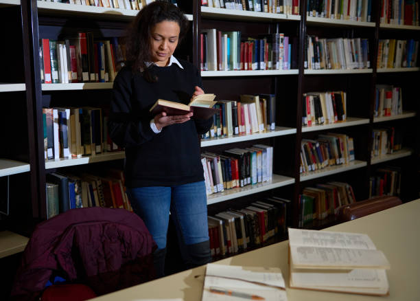 istock Young woman reading a book in a quiet library setting 2195933857