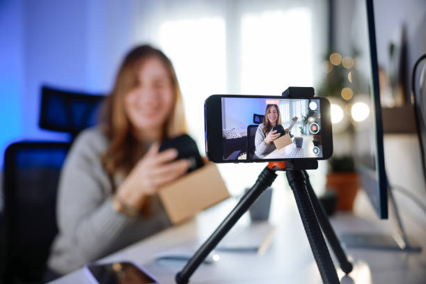 istock Female blogger unboxing parcel with tech product using smartphone on tripod, recording video content for tech blog at home 2195936925