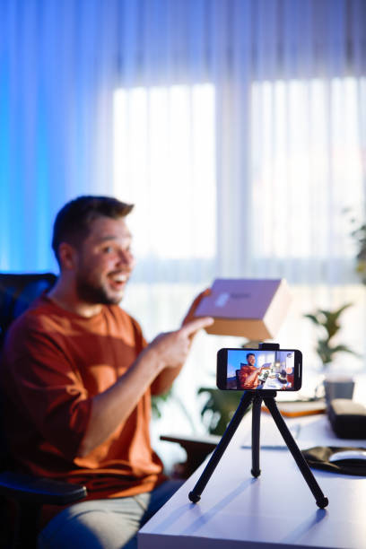 istock Male blogger unboxing parcel with tech product using smartphone on tripod, recording video content for tech blog at home 2195937088