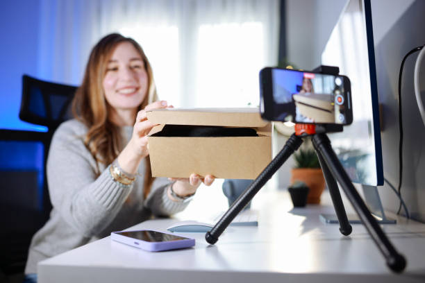 istock Female blogger unboxing parcel with tech product using smartphone on tripod, recording video content for tech blog at home 2195938276
