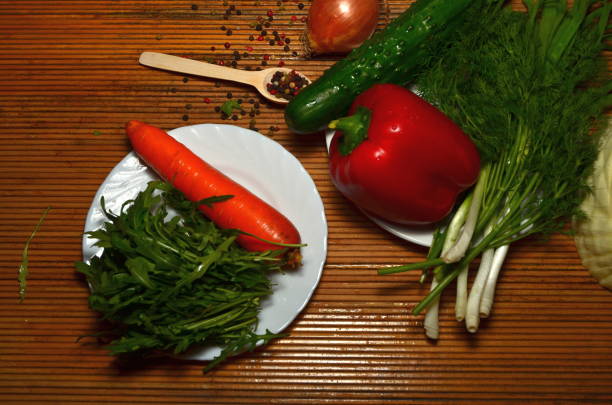 fresh vegetables of different types on a dark background for salad grass rakula tomatoes peppers wooden spoon onion cabbage carrots and other vegetables tomato, sweet pepper, greens, cucumber, light wooden spoon, onion, arugula herb with meat taste