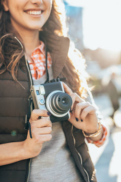 Close up of girl photographer  with camera in her hands taking photos in the city. She is wearing casual clothing, taking photos with her beautiful analog film camera. Close-up image of urban female photographer