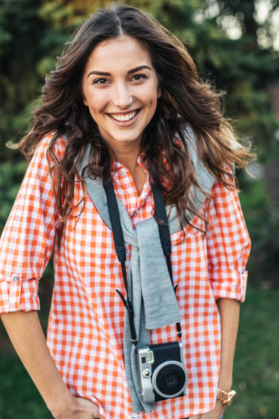 Beautiful girl photographer with camera looking at camera and smiling. She is wearing casual clothing, taking photos with her beautiful analog film camera. Close-up image of urban female photographer