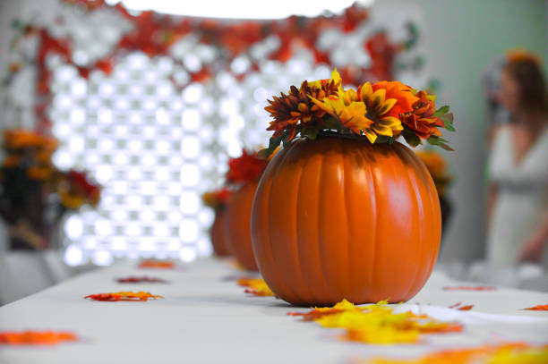 A beautiful homemade three-tier white wedding cake adorned with vibrant yellow sunflower decorations, red ribbons, and green vine-like embellishments. Captured in a cozy, home setting, this cake radiates rustic charm and personal creativity, perfect for an intimate fall wedding or celebration.
