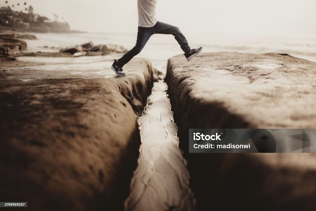 Child jumping over small river or stream by the ocean Little boy jumping over water on wet rocks taking a risk Jumping Stock Photo Child jumping over small river or stream by the ocean Little boy jumping over water on wet rocks taking a risk Jumping Stock Photo