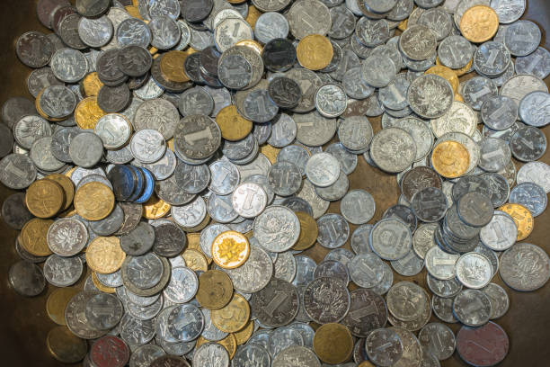 This image shows a pile of coins in circulation, featuring a mix of denominations and currencies. The coins are made of various metals, giving them different colors and textures. Some are silver, others are gold, and a few have a copper or bronze hue. The designs on the coins vary, with some displaying numbers and symbols, while others have more intricate patterns or portraits. This collection represents the everyday use of coins in transactions and the diversity of coins that people handle in daily life.