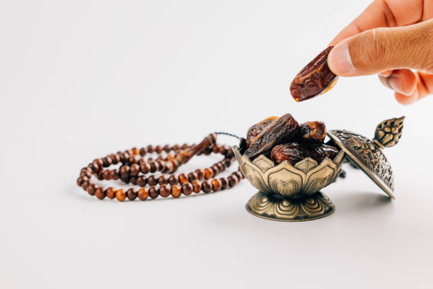 istock Holy Ramadan celebration with hands arranging dates and beads in ornate dish on white background as decoration 2195982338