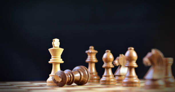 istock Last move in chess, check mate, brown king chess piece fallen down defeated with single off white beige cream king, against black background 2195984857