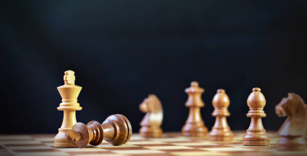 istock Last move in chess, check mate, victory, losing brown king chess piece fallen down lost, defeated, over black background, more chess pieces defocused in backdrop 2195986355