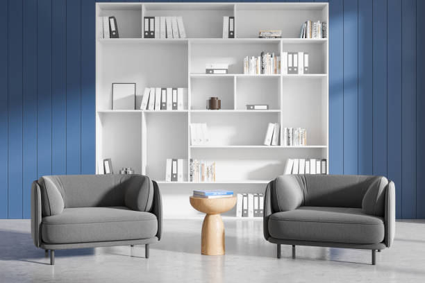 istock Modern office interior with grey armchairs, wooden table, and white bookshelf against blue panel wall. 3D Rendering 2195986970