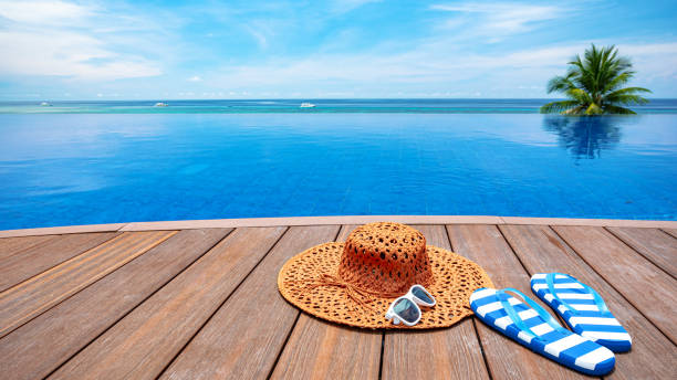 A cheerful woman in a striped swimsuit leans on the edge of a vibrant blue swimming pool under a bright summer sky with soft clouds