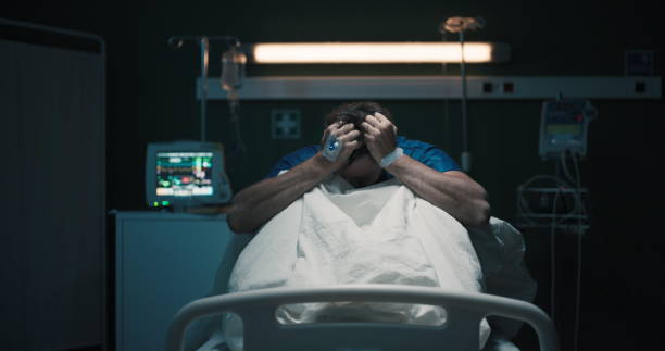 istock Exhausted tired man with headache suffering from migraine holding head with hands sitting on hospital bed 2195991663