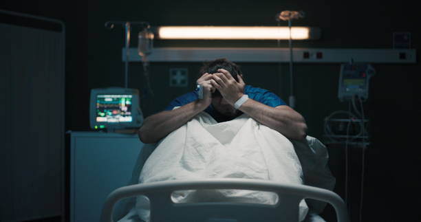 istock Exhausted tired man with headache suffering from migraine holding head with hands sitting on hospital bed 2195991686