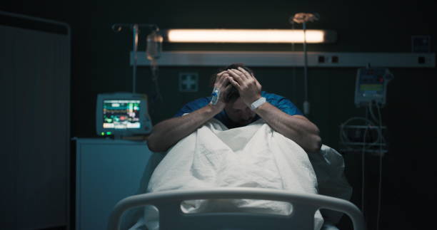 istock Exhausted tired man with headache suffering from migraine holding head with hands sitting on hospital bed 2195993065