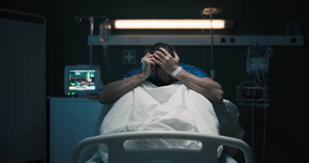 istock Exhausted tired man with headache suffering from migraine holding head with hands sitting on hospital bed 2195993079