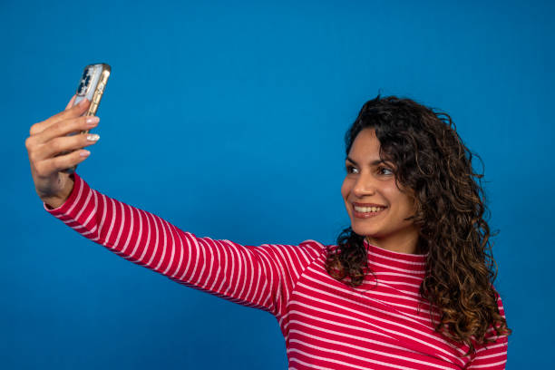 istock Young latin woman taking a selfie with smartphone on blue background 2195993619