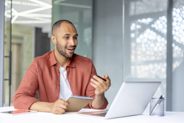 istock Man at workplace watching training video online seminar webinar, businessman with notepad writing down data while sitting inside office with laptop 2196000073