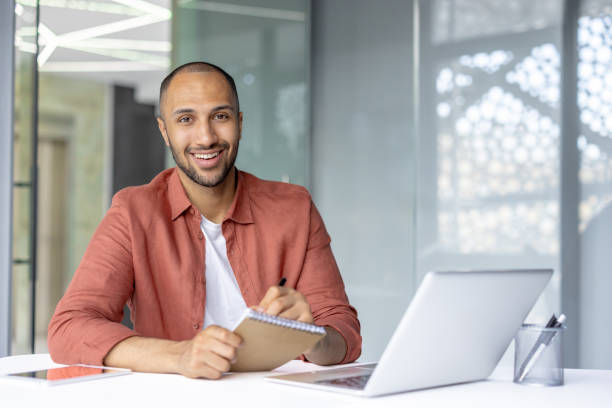 istock Smiling professional taking notes at a desk with laptop in office 2196000081