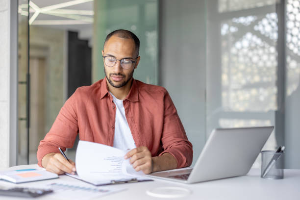 istock Focused businessman reviewing documents at modern office desk with laptop 2196000084