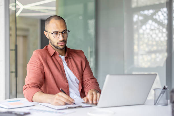 istock Focused professional working on a laptop and taking notes at a desk 2196000089