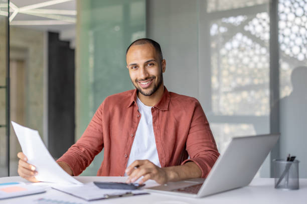 istock Smiling businessman reviewing documents at his office desk with a laptop 2196000099