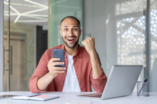 istock Excited man celebrates success with smartphone in modern office setting 2196000148