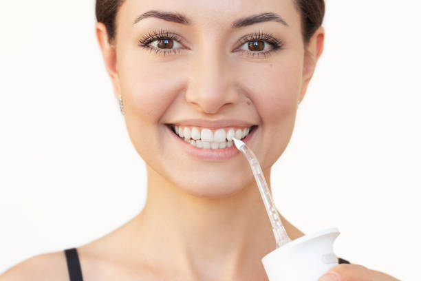 istock Young woman brushing her teeth with a white portable irrigator and looking at camera. 2196000549