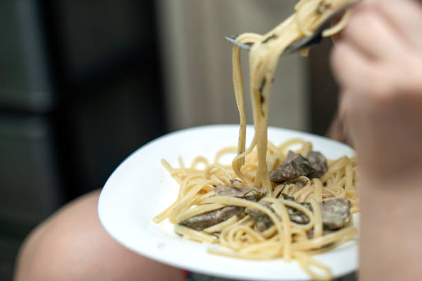 people enjoys flat linguine pasta with fried beef liver and herbs, skillfully twirling it around her fork before taking a bite, showcasing a delightful culinary moment