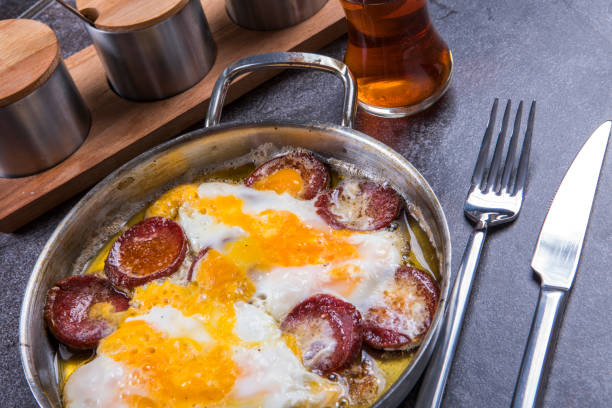 Turkish spicy sausage with eggs (sucuklu yumurta) side of a Turkish tea is a timeless classic of Turkish breakfasts, loved for its rich flavors and simplicity. The sizzling slices of spicy sausage combined with perfectly cooked eggs create a visually stunning and appetizing dish. This photograph highlights the golden yolks of the eggs nestled among the crispy, aromatic sausage slices in a hot pan. With its inviting colors and comforting presentation, this image is perfect for food blogs, recipe websites, social media posts, or any project showcasing the beauty and flavors of traditional Turkish cuisine.