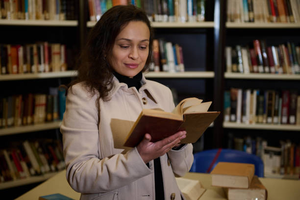 istock Woman reading a book in a library with shelves in the background 2196010790