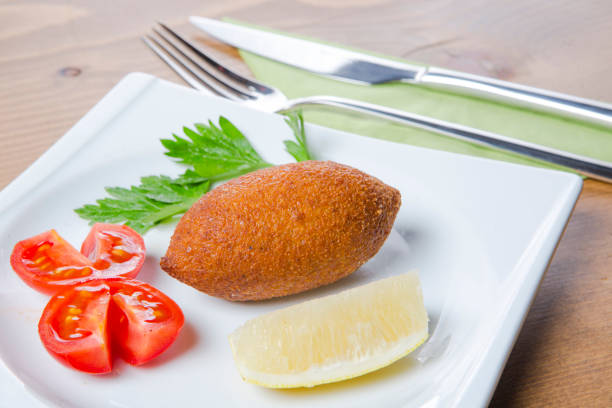 A delicious classic of Turkish cuisine, stuffed meatballs (içli köfte) are elegantly served with fresh tomato slices and vibrant lemon wedges. The crispy golden shell and hearty filling perfectly complement the refreshing acidity of lemon and the juicy sweetness of tomatoes. Ideal for food blogs, restaurant menus, or culinary promotions.