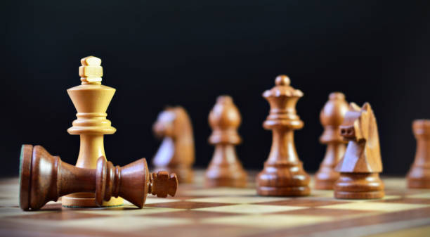 istock Last move in chess, check mate, victory, brown king chess piece fallen down defeated, over black background, several other chess pieces defocused in backdrop 2196016497